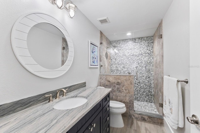 bathroom with toilet, hardwood / wood-style flooring, vanity, and tiled shower