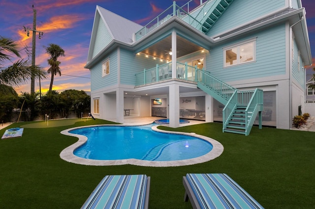 back house at dusk with a balcony, a patio, and a yard