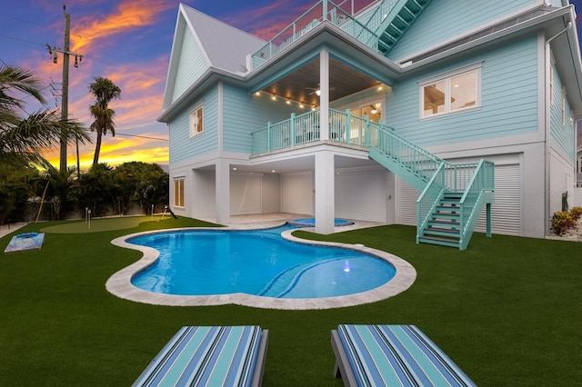 back house at dusk featuring a lawn, a balcony, and a patio area