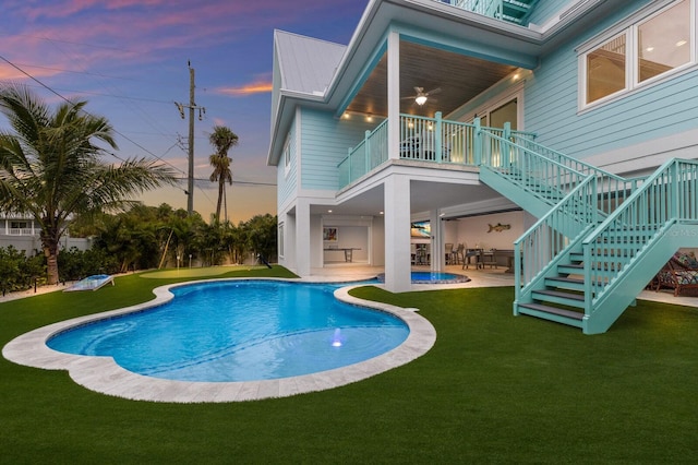 pool at dusk with ceiling fan, a yard, and a patio