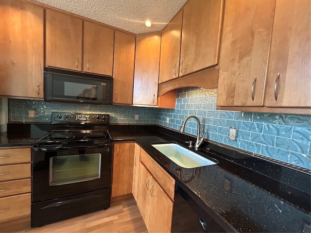 kitchen with a textured ceiling, dark stone counters, light hardwood / wood-style flooring, black appliances, and sink