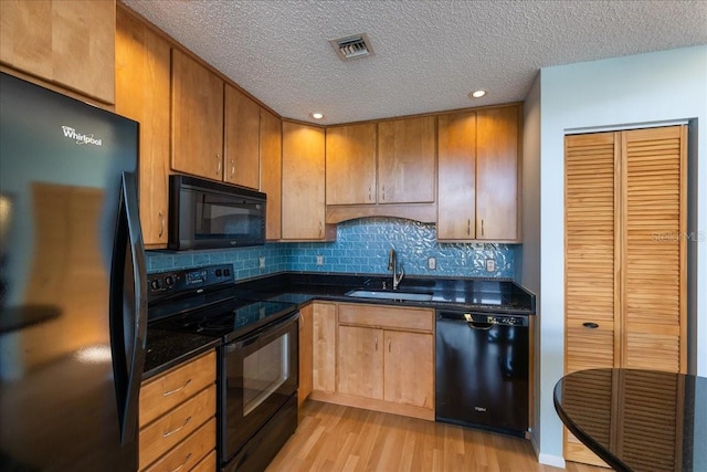 kitchen featuring tasteful backsplash, dark stone countertops, black appliances, light hardwood / wood-style floors, and sink