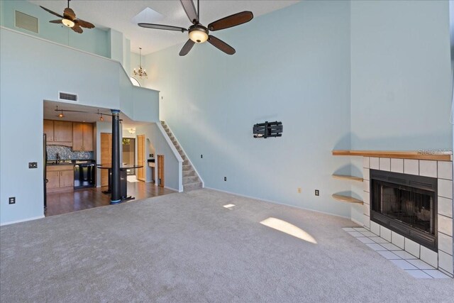 unfurnished living room featuring a towering ceiling, a tiled fireplace, light colored carpet, and ceiling fan