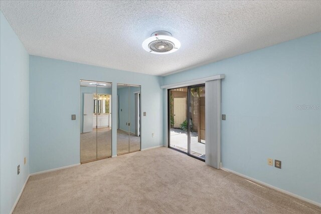 unfurnished bedroom with access to outside, a textured ceiling, an inviting chandelier, and light colored carpet