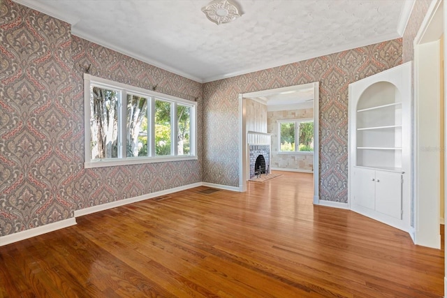 unfurnished living room featuring hardwood / wood-style flooring, built in shelves, a healthy amount of sunlight, and ornamental molding