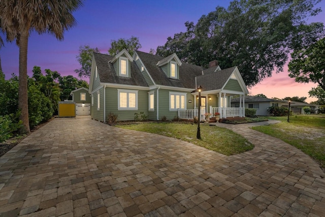 cape cod home featuring a lawn and covered porch