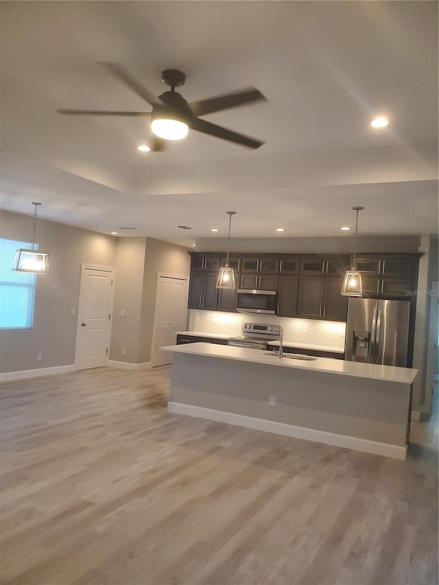 kitchen with light hardwood / wood-style flooring, a center island with sink, stainless steel appliances, and ceiling fan