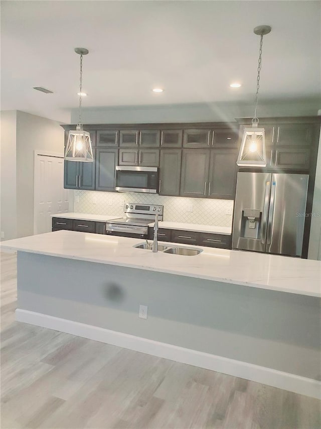 kitchen with a sink, decorative light fixtures, tasteful backsplash, stainless steel appliances, and light wood-style floors