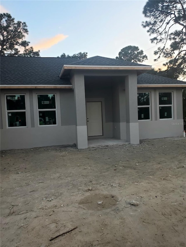 back of property at dusk featuring stucco siding and a shingled roof