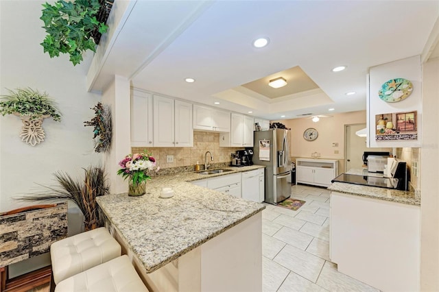 kitchen with stainless steel fridge, sink, white cabinets, a breakfast bar, and tasteful backsplash