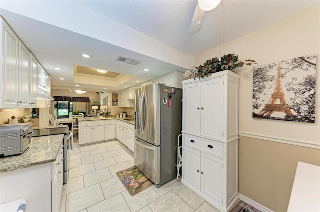 kitchen with stainless steel fridge, ceiling fan, backsplash, a tray ceiling, and white cabinetry