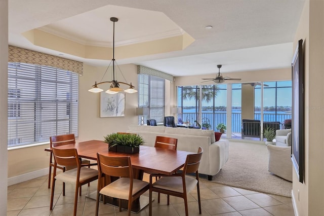 dining space featuring ornamental molding, a raised ceiling, ceiling fan, a water view, and light tile patterned flooring