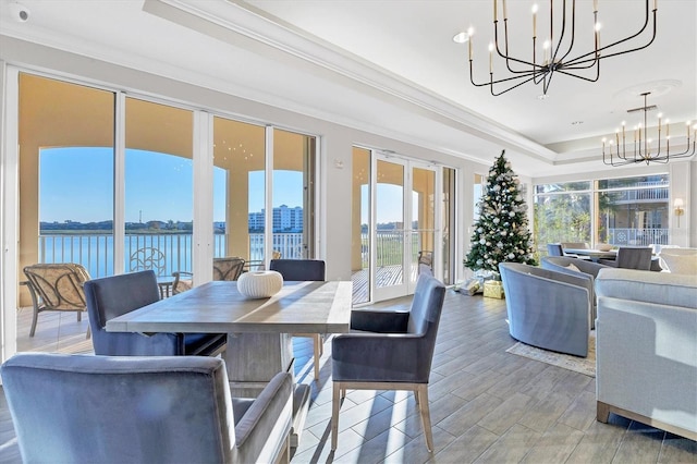 dining room with a tray ceiling, crown molding, a water view, a notable chandelier, and hardwood / wood-style floors