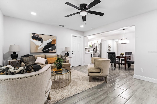 living room with ceiling fan with notable chandelier and light hardwood / wood-style flooring