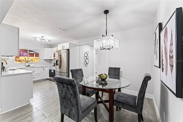 dining room with light wood-type flooring, an inviting chandelier, sink, and a textured ceiling