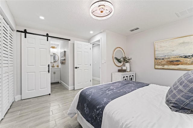 bedroom featuring light wood-type flooring, a textured ceiling, ensuite bathroom, and a barn door