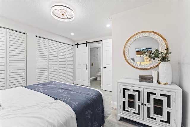 bedroom featuring a textured ceiling, a barn door, hardwood / wood-style floors, and two closets