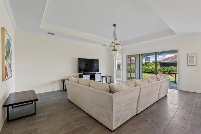 living room featuring a tray ceiling, ornamental molding, and a notable chandelier