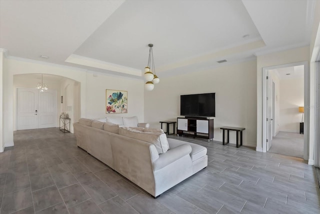 living room featuring a chandelier, a tray ceiling, and crown molding