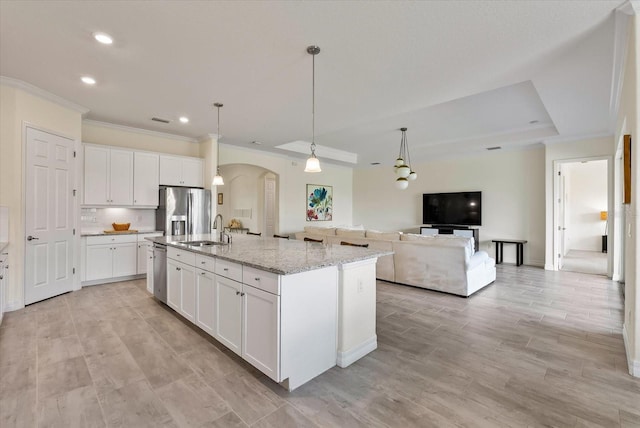 kitchen with white cabinetry, sink, stainless steel appliances, light stone counters, and a kitchen island with sink