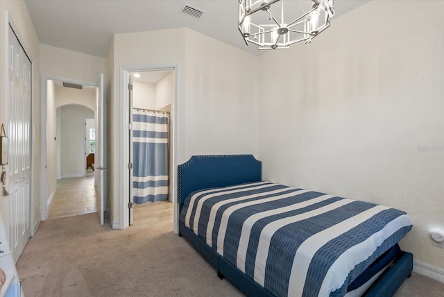 bedroom with a notable chandelier, ensuite bathroom, light carpet, and a closet