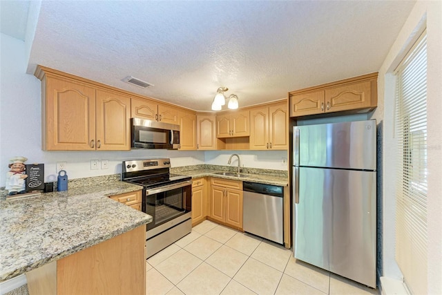 kitchen with sink, light tile floors, appliances with stainless steel finishes, light stone countertops, and a textured ceiling