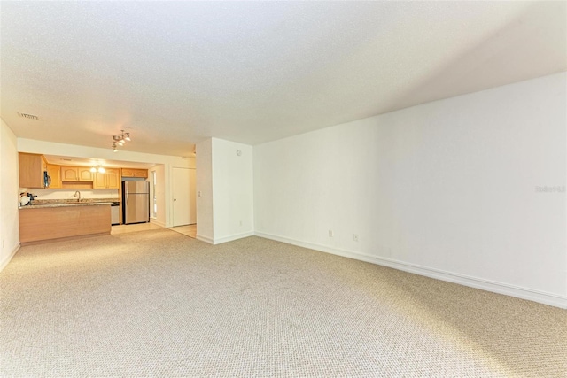 unfurnished living room with light carpet, a textured ceiling, and sink