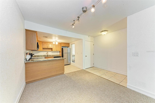 kitchen with stove, stainless steel refrigerator, track lighting, light stone countertops, and light carpet