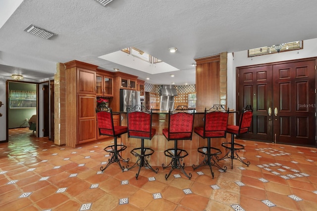 kitchen featuring a kitchen breakfast bar, a textured ceiling, stainless steel refrigerator with ice dispenser, and light tile floors