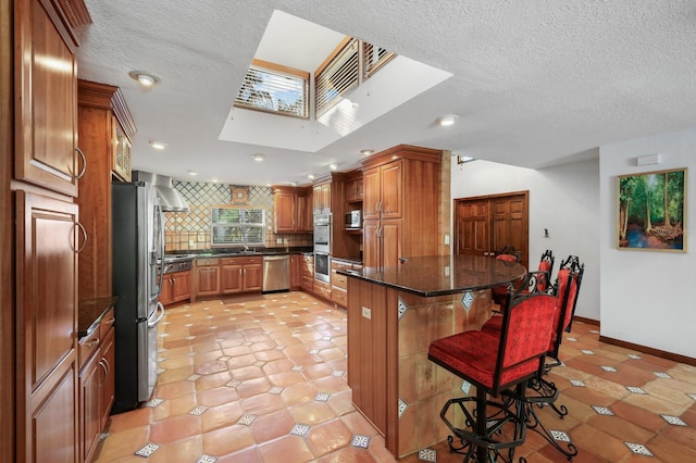 kitchen with light tile floors, appliances with stainless steel finishes, backsplash, a breakfast bar area, and wall chimney exhaust hood