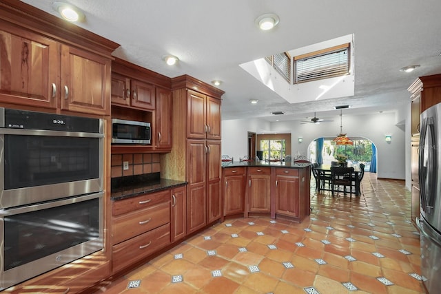 kitchen featuring hanging light fixtures, ceiling fan, stainless steel appliances, dark stone countertops, and tasteful backsplash