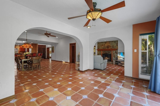 unfurnished living room with dark tile flooring, ceiling fan, and a stone fireplace