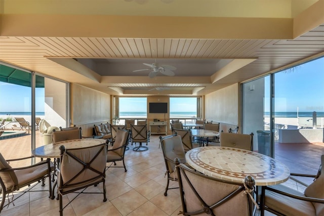 tiled dining space featuring a water view, expansive windows, ceiling fan, and a raised ceiling