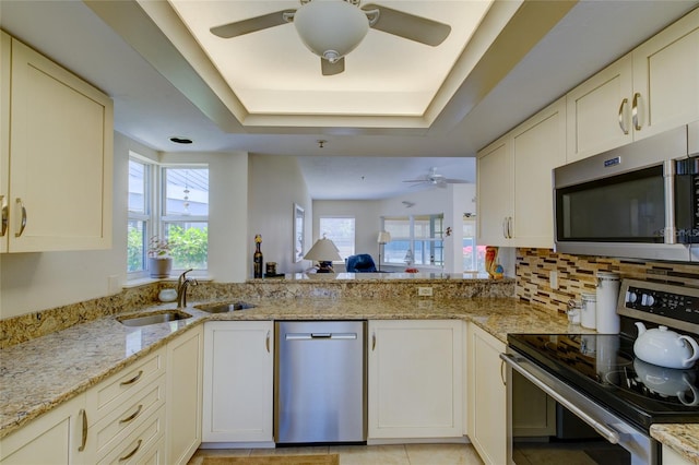 kitchen featuring ceiling fan, light stone countertops, stainless steel appliances, and a raised ceiling