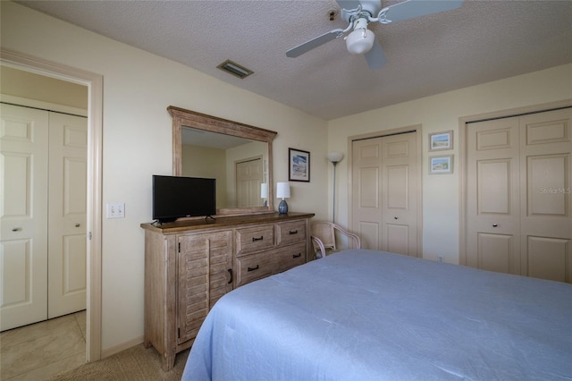 tiled bedroom featuring multiple closets, ceiling fan, and a textured ceiling