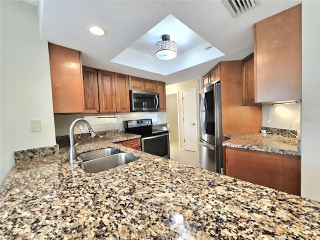 kitchen with stone counters, a tray ceiling, sink, and stainless steel appliances