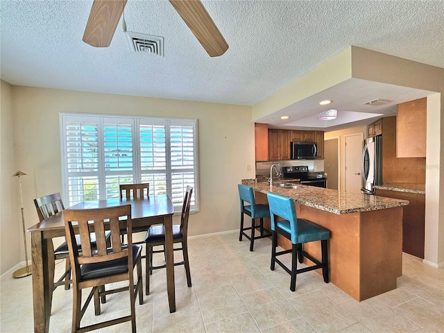 interior space with kitchen peninsula, stainless steel appliances, ceiling fan, and dark stone counters