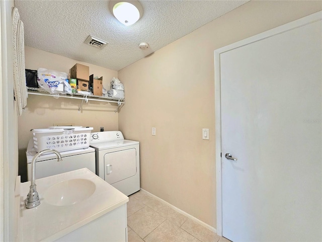 clothes washing area with light tile floors, washer and clothes dryer, a textured ceiling, and sink