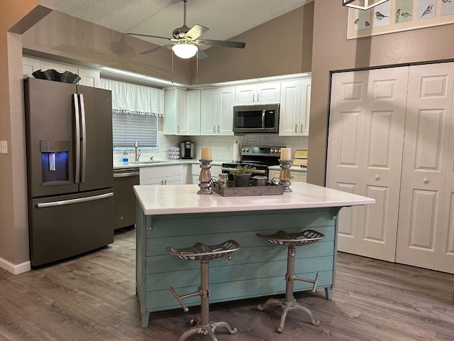 kitchen with hardwood / wood-style flooring, a kitchen bar, stainless steel appliances, and white cabinetry