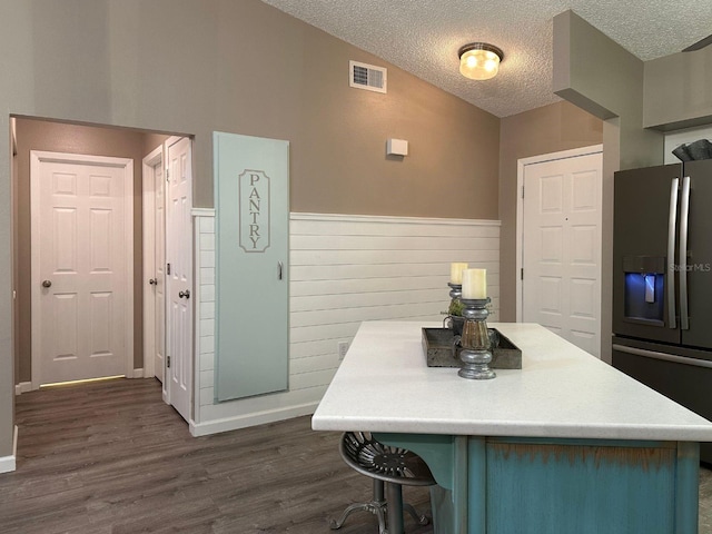 kitchen with a textured ceiling, dark hardwood / wood-style floors, a breakfast bar area, and stainless steel refrigerator with ice dispenser