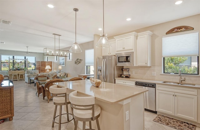 kitchen featuring pendant lighting, light tile floors, a kitchen island, a kitchen bar, and appliances with stainless steel finishes