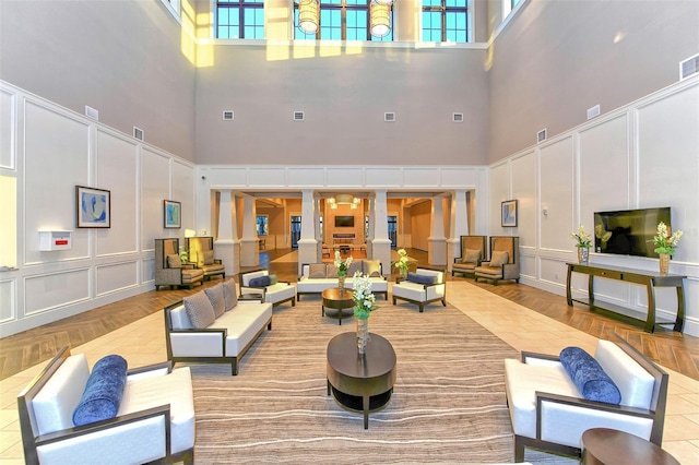 living room featuring light parquet flooring, decorative columns, and a towering ceiling