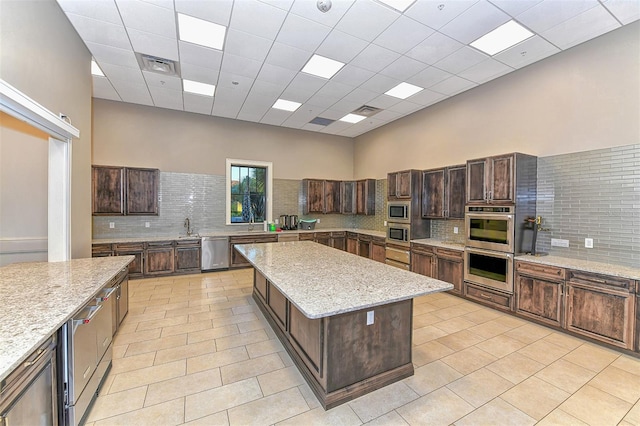 kitchen with light tile floors, appliances with stainless steel finishes, a kitchen island, and backsplash