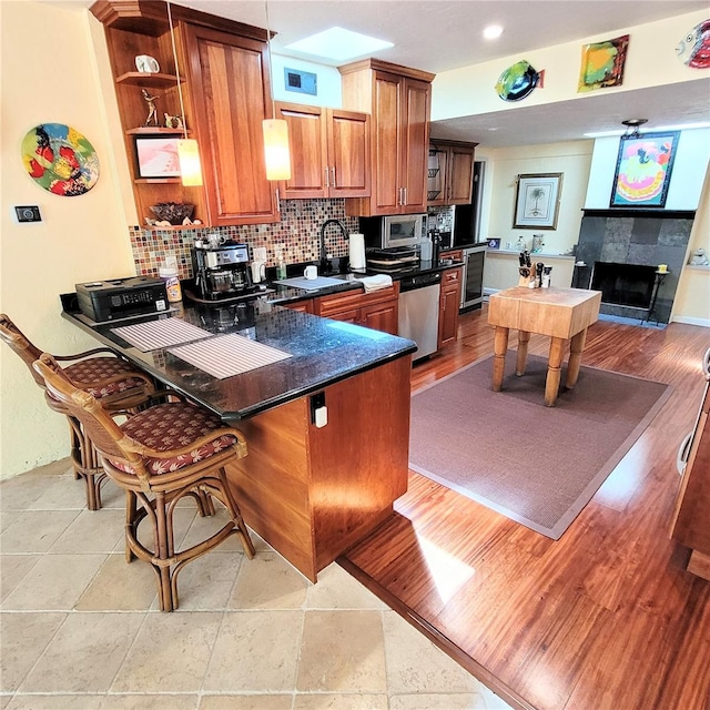 kitchen with kitchen peninsula, backsplash, stainless steel appliances, light tile floors, and a tile fireplace