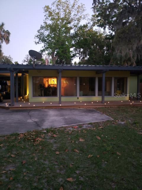 back house at dusk featuring a lawn and a patio area