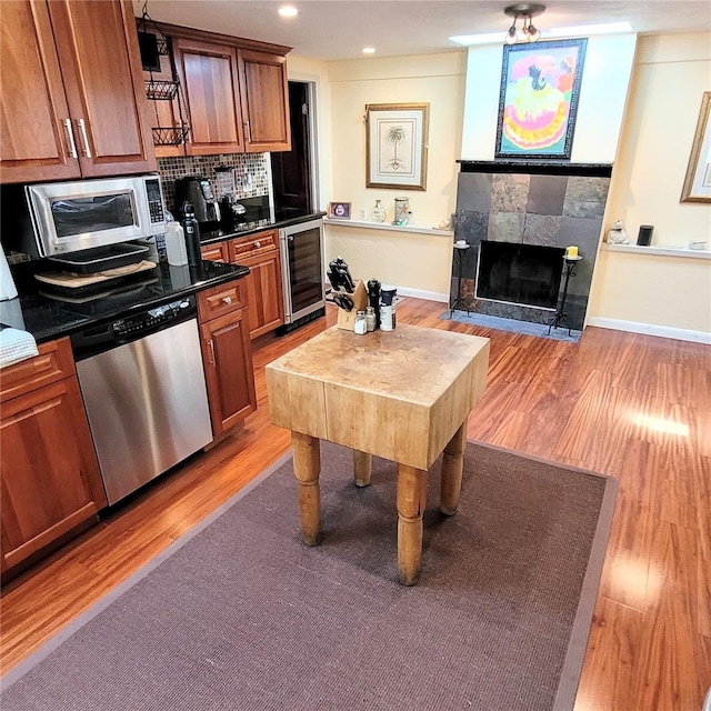 kitchen featuring a tile fireplace, light hardwood / wood-style floors, stainless steel appliances, wine cooler, and backsplash