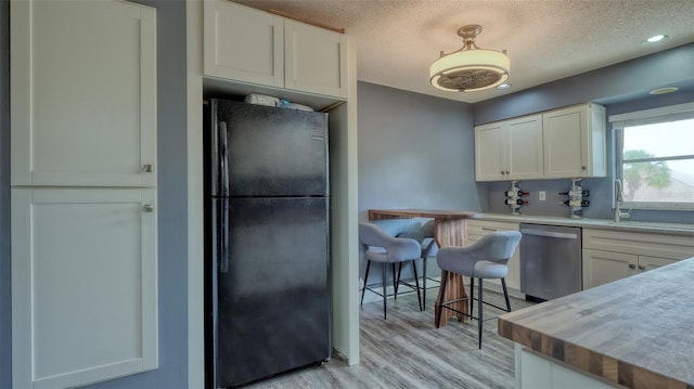 kitchen with black refrigerator, white cabinets, light wood-type flooring, stainless steel dishwasher, and a textured ceiling