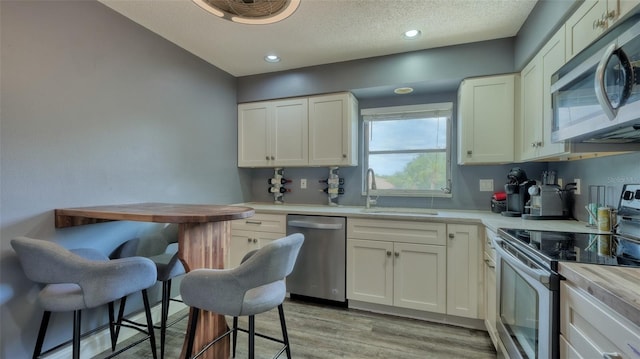 kitchen featuring appliances with stainless steel finishes, a textured ceiling, sink, light hardwood / wood-style floors, and white cabinetry