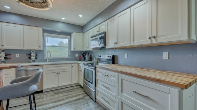 kitchen with appliances with stainless steel finishes, butcher block counters, light wood-type flooring, and white cabinetry