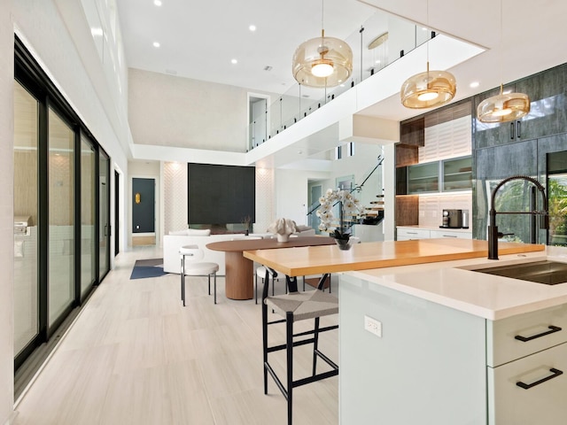 kitchen featuring white cabinets, hanging light fixtures, a breakfast bar, a high ceiling, and sink